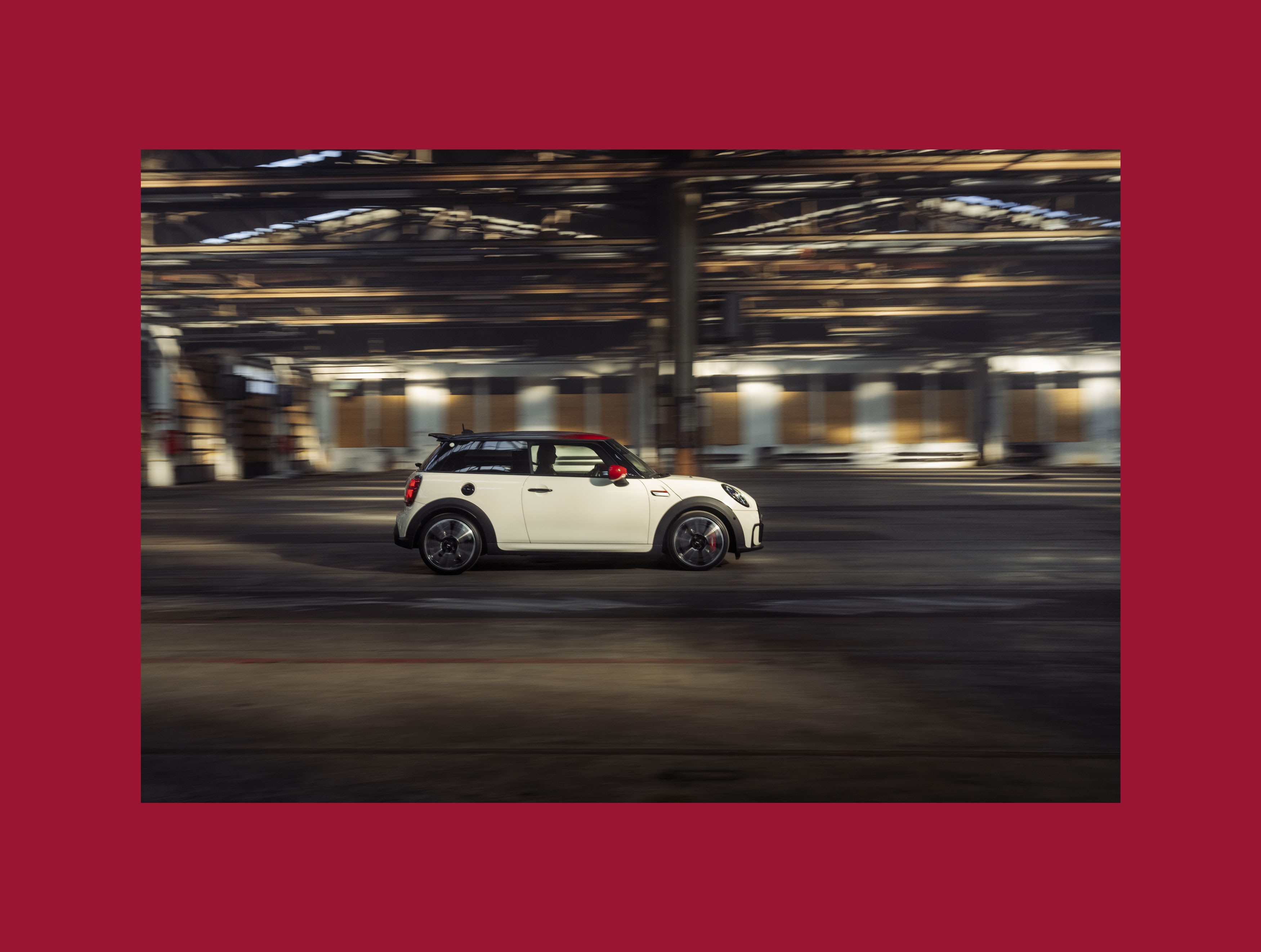 On a red background the following is placed: A fully side view of a driving John Cooper Works in the color Pepper White, from the Pat Moss Edition.